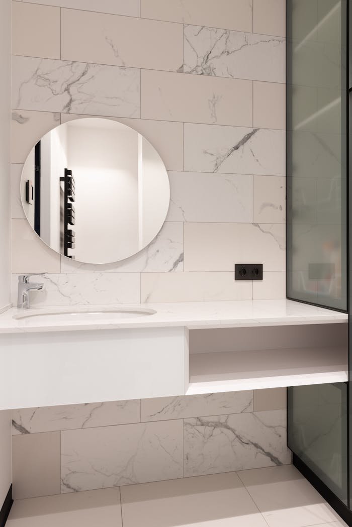 Interior of modern bathroom with marble tiled walls and round mirror over sink